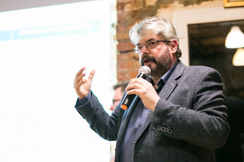 A man with a microphone making a point, a projected slide behind him