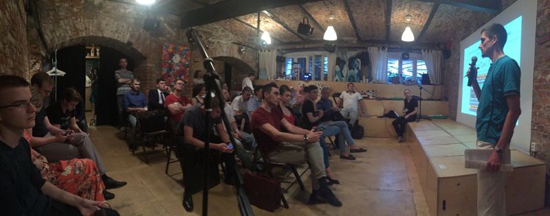 A wide view of a full room at The Yellow Door, a founder presenting beside a projected slide